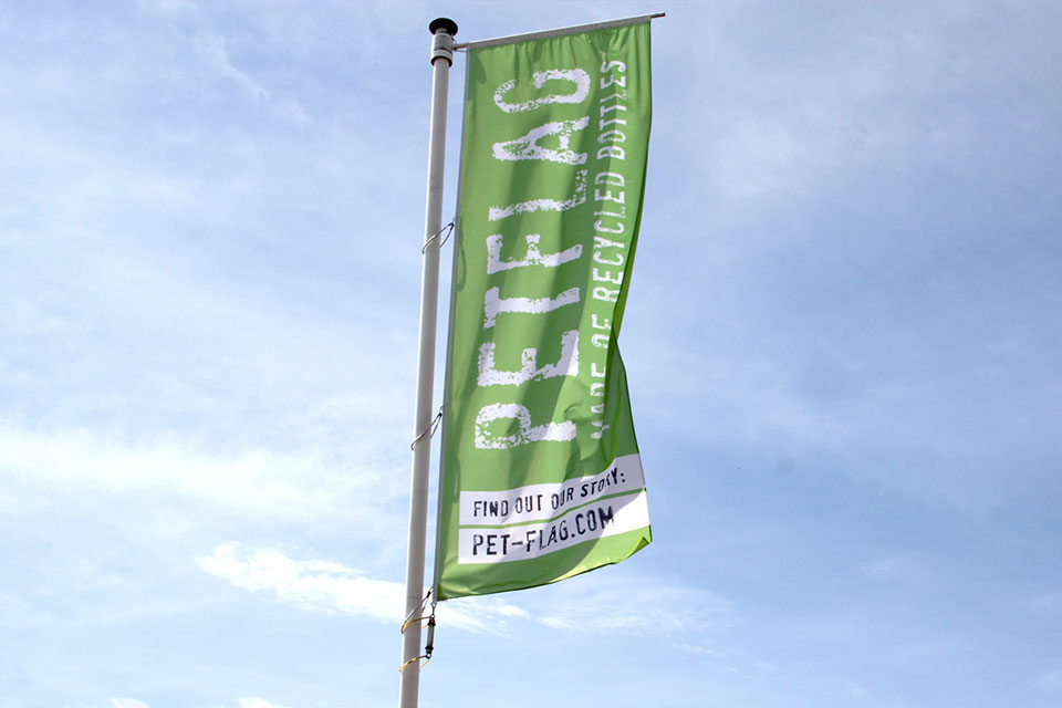 Vlag gemaakt van gerecyclede petflessen in vlaggemast, tegen een blauwe lucht
