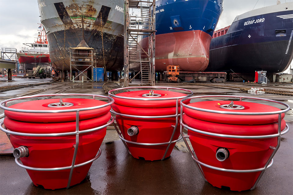 Drie  floating oil recovery units in de haven op de achtegrond drie grote schepen